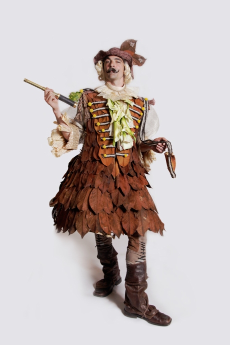 The jacket is made from Magnolia leaves attached to a framework of Seagrass decorated with a braid of Mongolian horse and goat rope, yellow Billy Button flowers, white Calla Lilies, Corn Husks and natural mesh. His hair is made from Sisal attached to a straw hat. The boot chaps are from the sleeves of an old leather jacket.